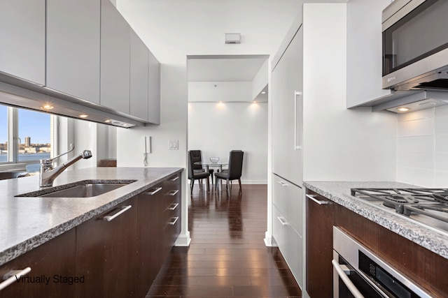 kitchen with appliances with stainless steel finishes, modern cabinets, a sink, light stone countertops, and dark wood-style floors