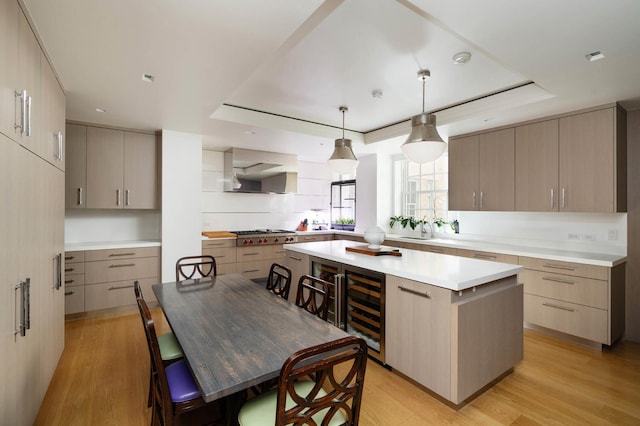 kitchen with wall chimney exhaust hood, wine cooler, light wood-style floors, and a center island