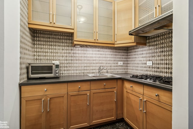 kitchen featuring dark countertops, under cabinet range hood, stainless steel gas cooktop, and a sink