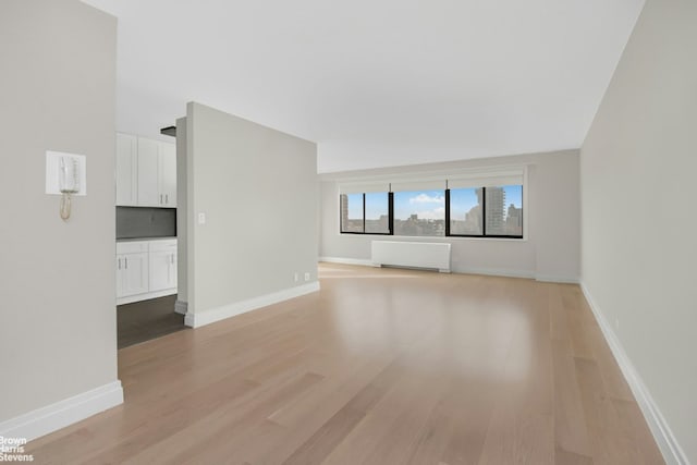 unfurnished living room featuring radiator heating unit and light hardwood / wood-style flooring