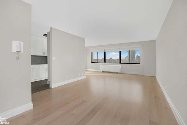 unfurnished living room featuring light wood-type flooring, radiator, and baseboards