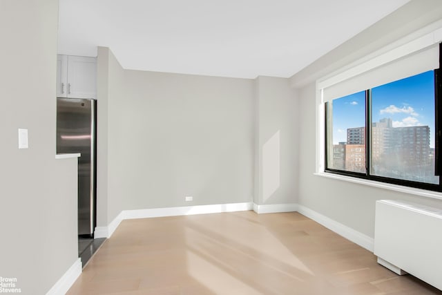 spare room with baseboards, radiator, a city view, and light wood-style flooring