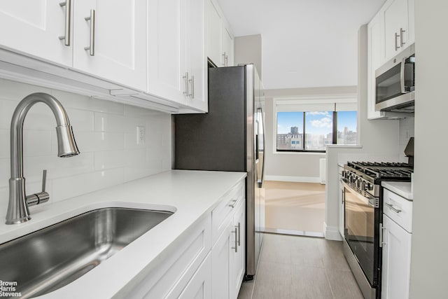 kitchen with stainless steel appliances, white cabinetry, a sink, and tasteful backsplash