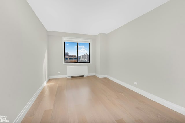 empty room with light wood finished floors, radiator heating unit, and baseboards