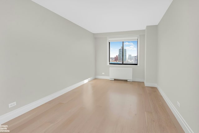 empty room featuring light wood-type flooring, baseboards, and radiator heating unit