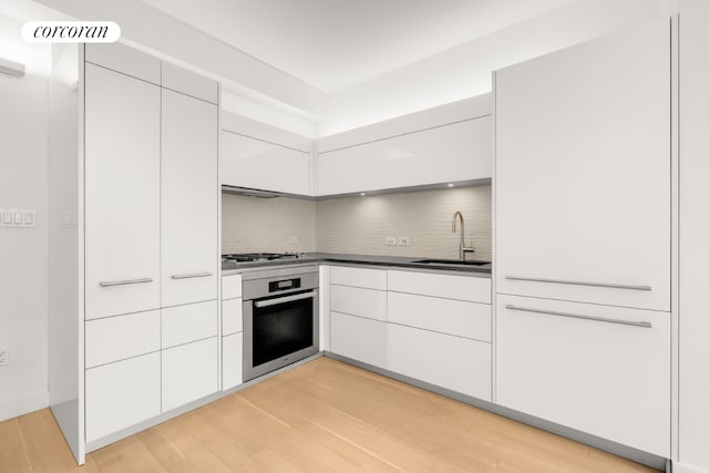 kitchen featuring sink, white cabinetry, light wood-type flooring, stainless steel appliances, and decorative backsplash