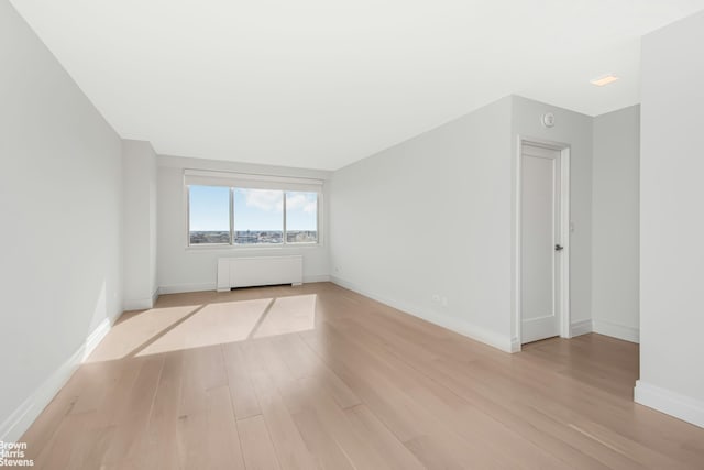 empty room with light wood finished floors, radiator, and baseboards