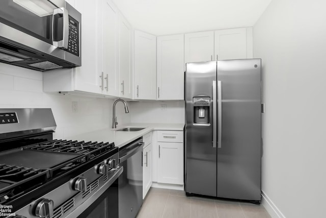 kitchen featuring sink, light tile patterned floors, appliances with stainless steel finishes, white cabinetry, and backsplash