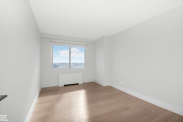 spare room featuring radiator, wood finished floors, and baseboards