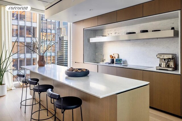 100 E 53rd St Unit 31B, New York City, NY 10022 - kitchen featuring tasteful backsplash, black electric cooktop, a kitchen breakfast bar, a kitchen island, and light hardwood / wood-style floors