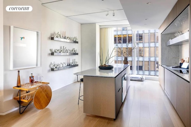 kitchen with rail lighting, a breakfast bar, a kitchen island, a wall of windows, and light hardwood / wood-style floors