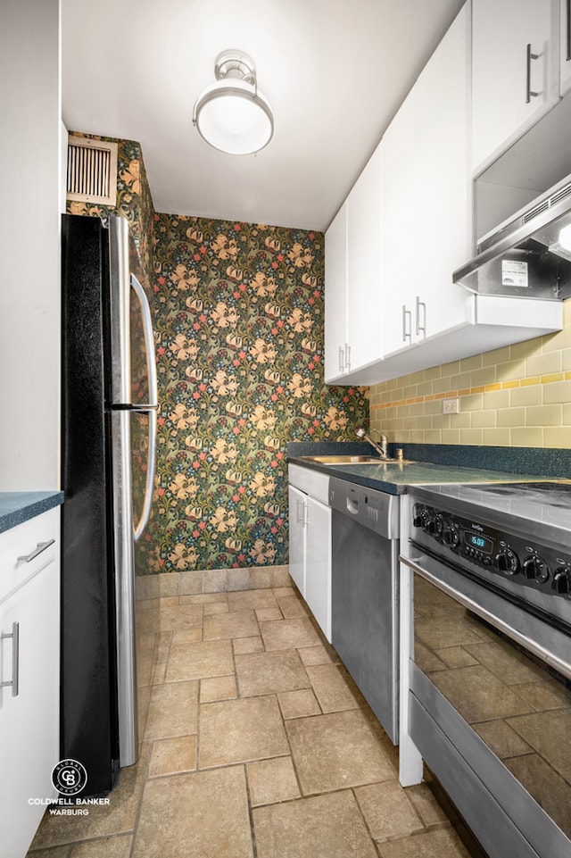 kitchen with appliances with stainless steel finishes, wallpapered walls, dark countertops, baseboards, and white cabinetry