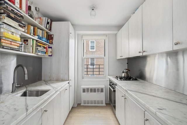 kitchen featuring light stone countertops, a sink, radiator, open shelves, and stainless steel gas stovetop