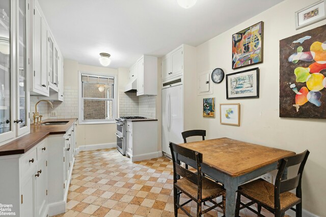 kitchen featuring built in fridge, white cabinetry, sink, backsplash, and double oven range