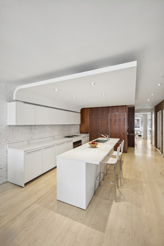 kitchen with a center island with sink, light wood-type flooring, white cabinets, a breakfast bar, and sink