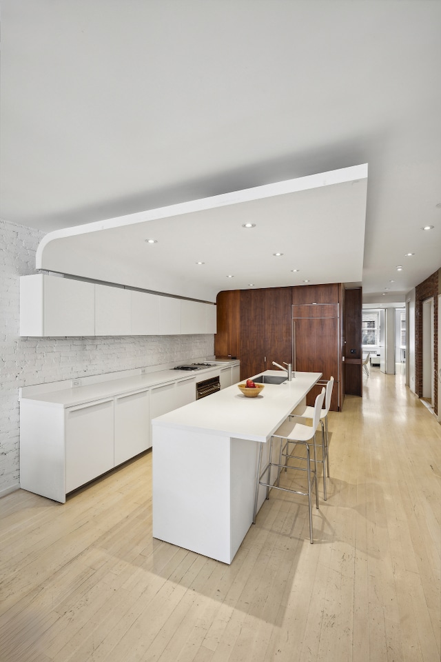 kitchen with backsplash, white cabinets, a sink, modern cabinets, and light wood-type flooring