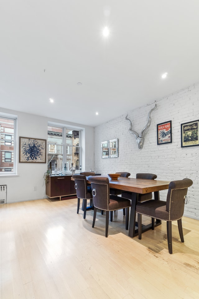 dining space with brick wall, light wood finished floors, and radiator heating unit