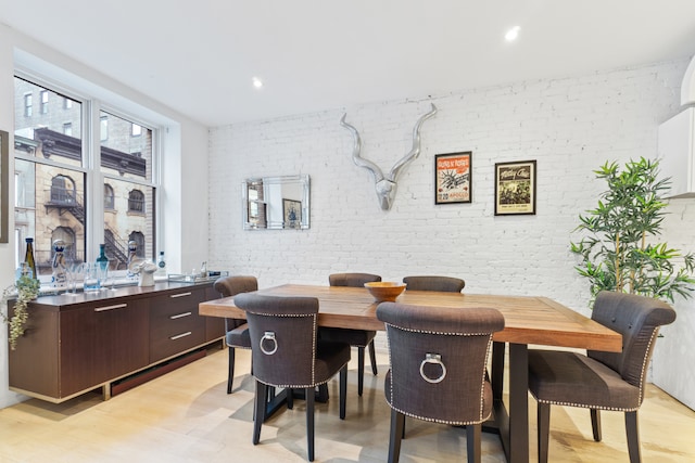 dining room featuring light wood-style floors, recessed lighting, and brick wall