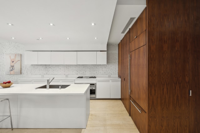 kitchen featuring backsplash, gas cooktop, sink, white cabinetry, and stainless steel oven