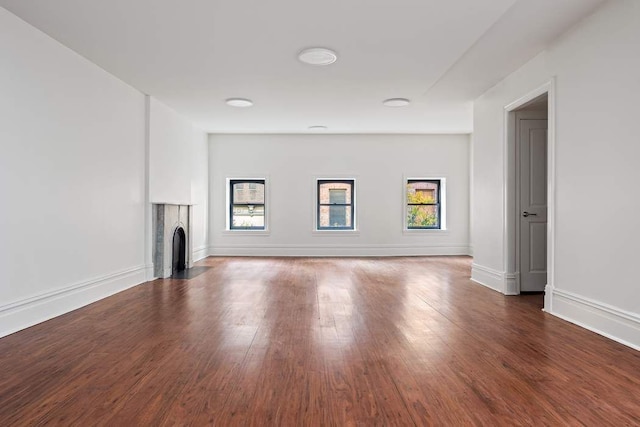 unfurnished living room with a fireplace with flush hearth, wood finished floors, and baseboards