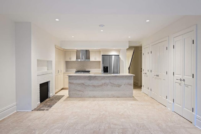 kitchen with wall chimney exhaust hood, stainless steel refrigerator with ice dispenser, a center island, light countertops, and cream cabinets