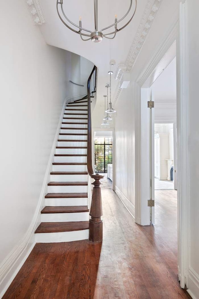 stairs with wood finished floors, a notable chandelier, baseboards, and a towering ceiling