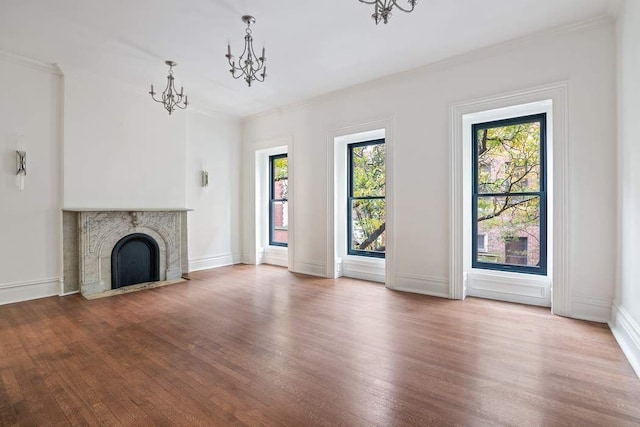 unfurnished living room with a tiled fireplace, wood finished floors, a notable chandelier, and ornamental molding