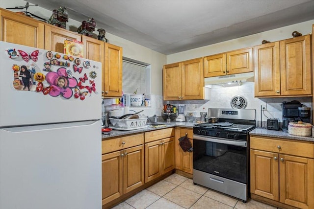 kitchen featuring white refrigerator, tasteful backsplash, dark stone counters, light tile patterned floors, and stainless steel gas range