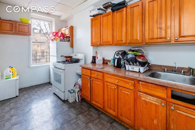 kitchen with brown cabinets, white appliances, a paneled ceiling, and a sink