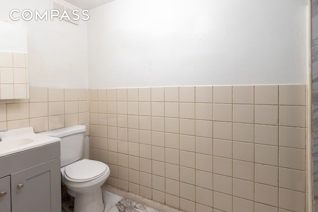 bathroom with vanity, tile walls, toilet, and a wainscoted wall