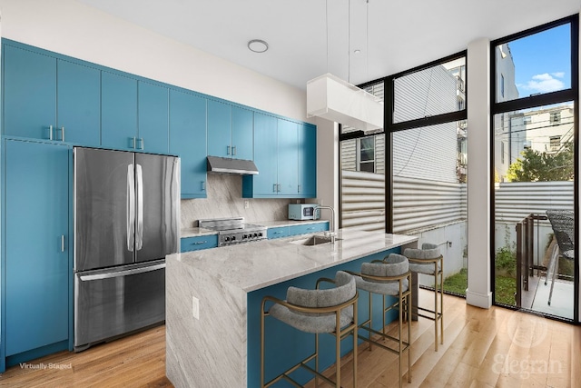 kitchen with stainless steel fridge, a breakfast bar, range, a center island with sink, and light wood-type flooring