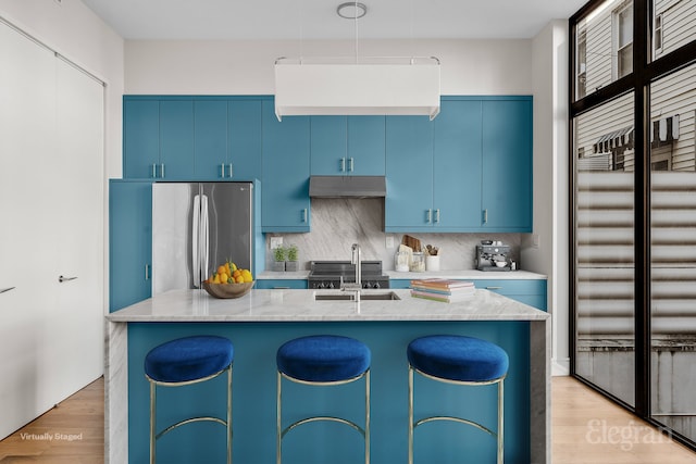 kitchen featuring light wood-style flooring, under cabinet range hood, blue cabinets, a sink, and freestanding refrigerator