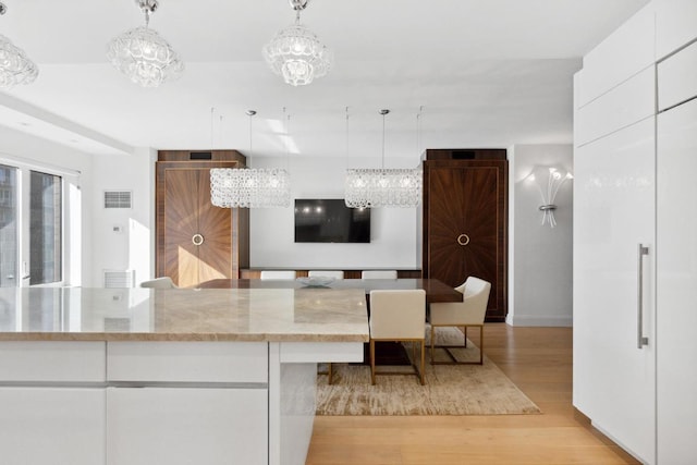 kitchen with white cabinetry, light wood-type flooring, pendant lighting, and a chandelier