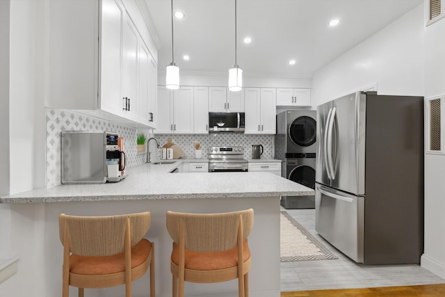 kitchen featuring stacked washer / drying machine, a peninsula, stainless steel appliances, white cabinetry, and a sink