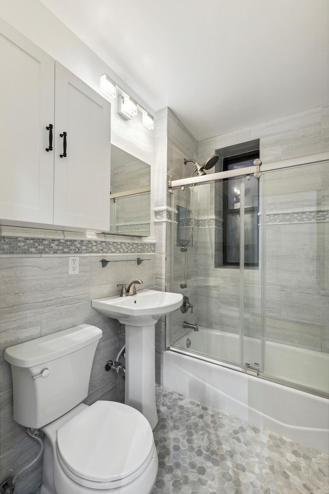 bathroom featuring tile walls, combined bath / shower with glass door, and toilet