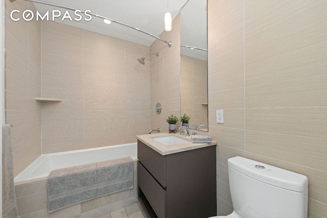 full bath featuring tiled shower / bath, vanity, toilet, and tile walls