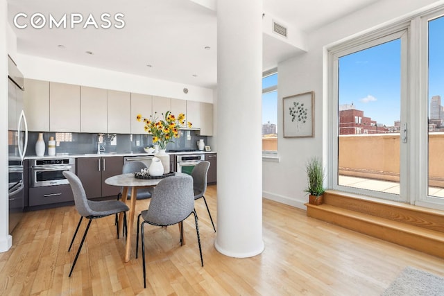 dining room featuring light wood-type flooring, baseboards, visible vents, and a city view