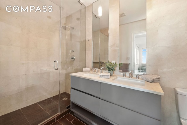 full bathroom featuring double vanity, a stall shower, toilet, a sink, and tile walls