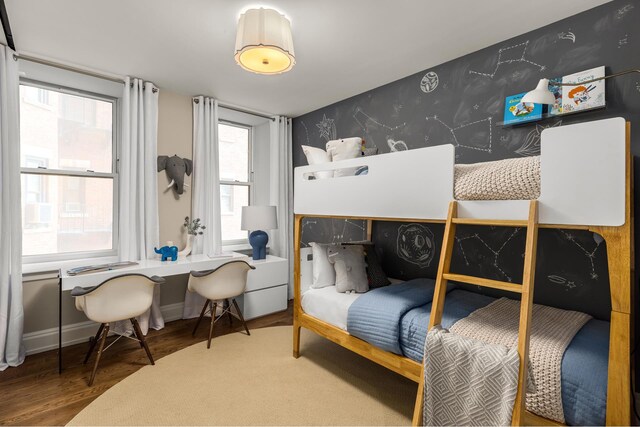 bedroom featuring an accent wall, multiple windows, wallpapered walls, and wood finished floors