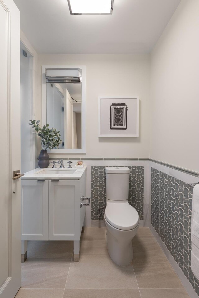 bathroom featuring toilet, vanity, a wainscoted wall, and tile walls