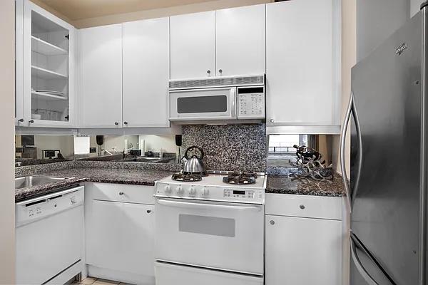 kitchen with white cabinetry, white appliances, and dark stone counters