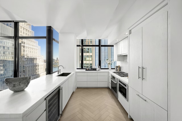 kitchen with wall oven, white cabinetry, a sink, modern cabinets, and beverage cooler