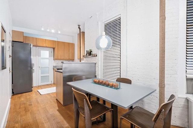 kitchen featuring light wood-type flooring, stainless steel refrigerator, track lighting, brick wall, and decorative backsplash