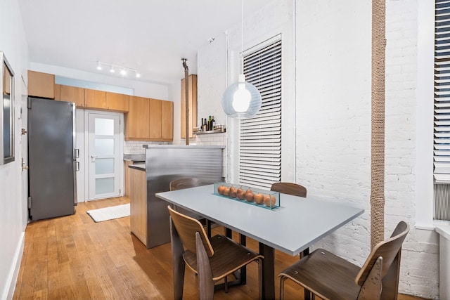 kitchen with decorative backsplash, brick wall, freestanding refrigerator, rail lighting, and light wood-type flooring