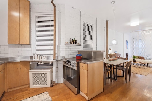 kitchen with light wood-style flooring, stainless steel countertops, decorative backsplash, light brown cabinetry, and stainless steel range with electric stovetop