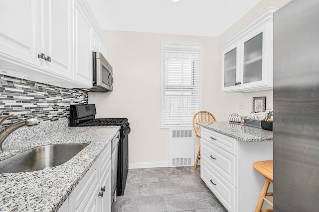 kitchen with backsplash, black gas stove, a sink, baseboards, and radiator