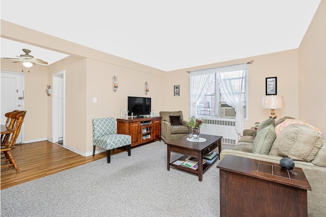 living area featuring light carpet, light wood-style flooring, radiator, a ceiling fan, and baseboards