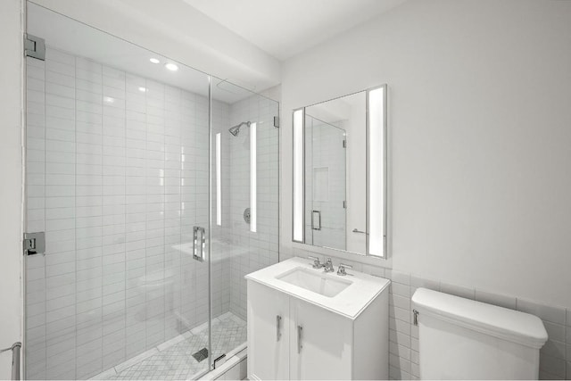 bathroom with vanity, toilet, a shower with shower door, and tile walls