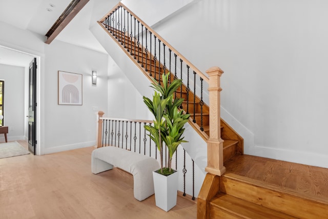 staircase featuring wood-type flooring and beamed ceiling