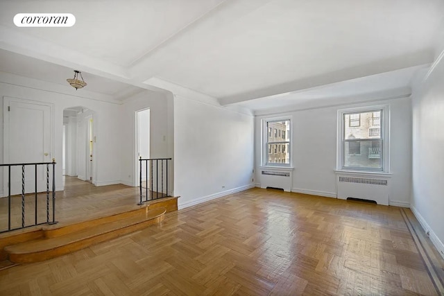 unfurnished room featuring radiator heating unit, visible vents, arched walkways, and baseboards